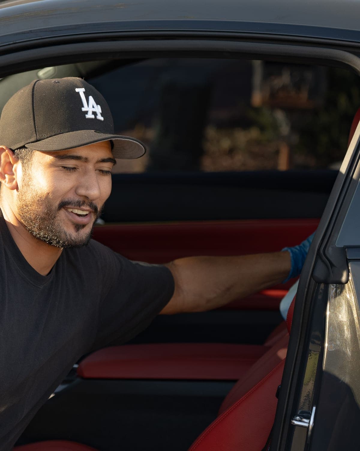 Nick wiping down the door card of a BMW M4, smiling, red leather interior behind him
